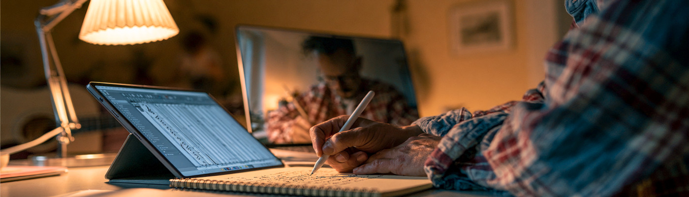 A music teacher writing notes on a tablet next to a laptop during an online lesson